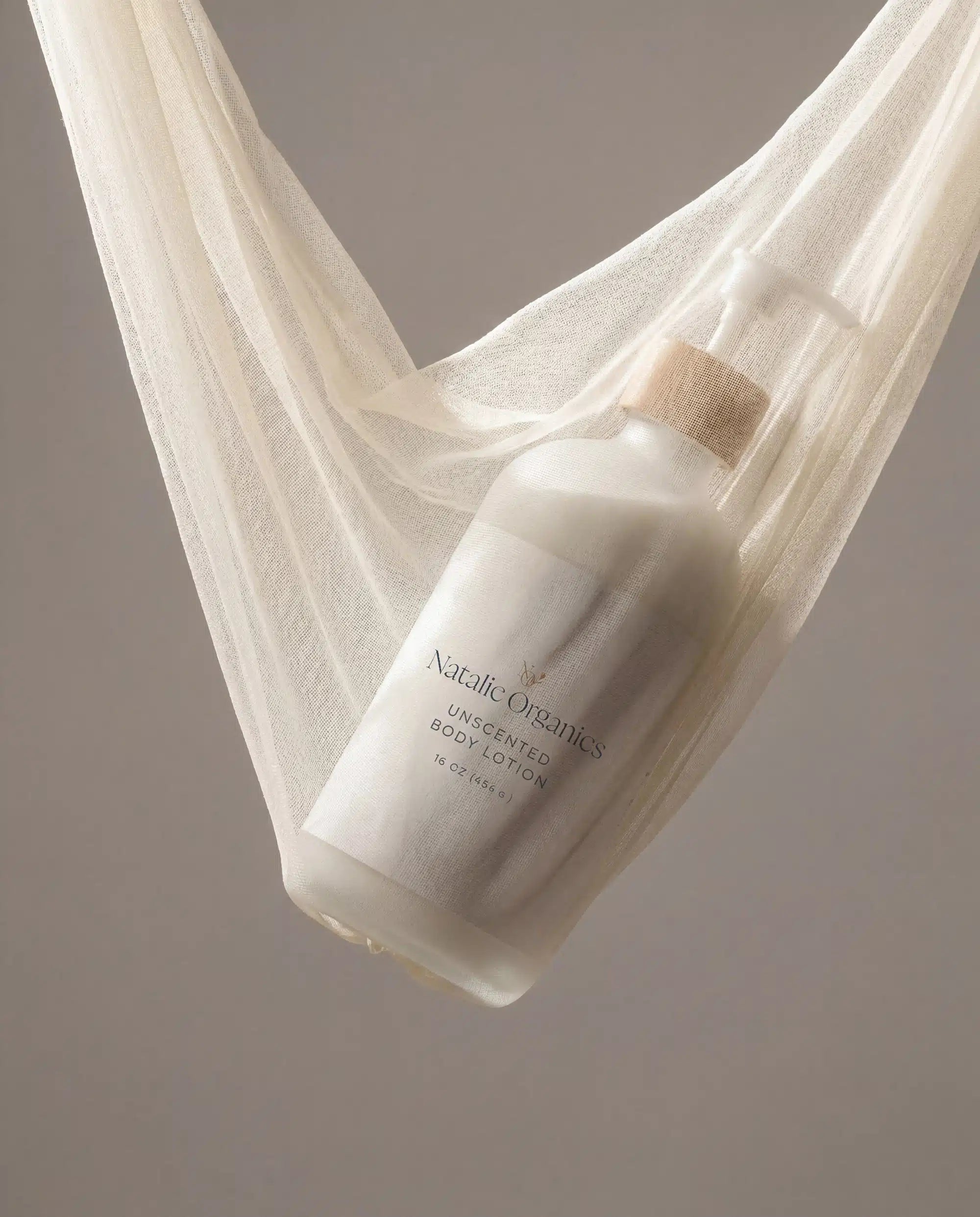 Body lotion pump bottle angled view with wooden pump, white bottle on sheer cloth